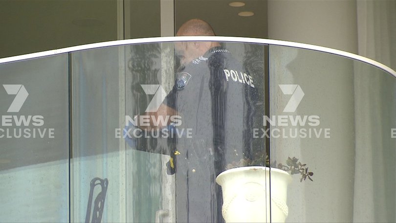 A forensic officer examines items on the apartment balcony as part of the ongoing investigation.
