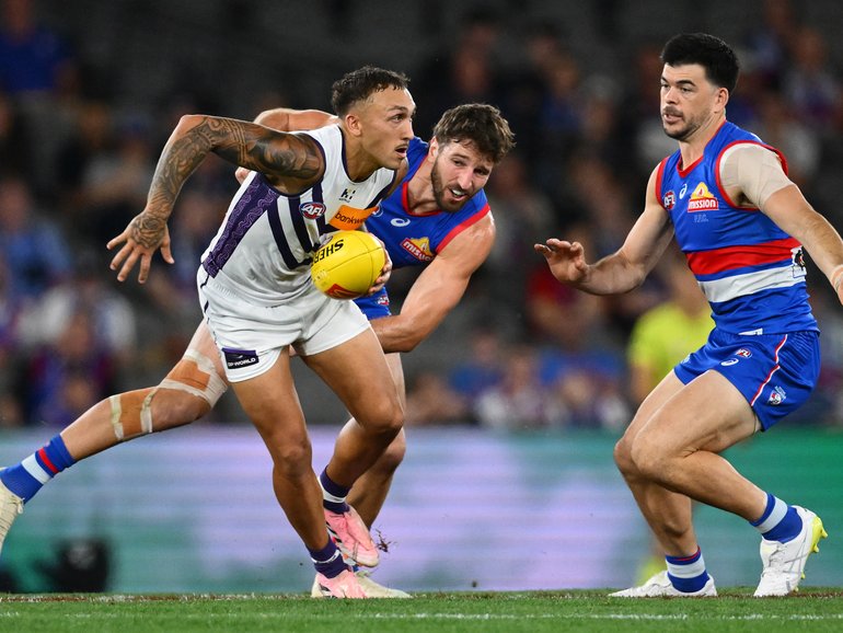 Shai Bolton of the Dockers handballs whilst being tackled by Marcus Bontempelli.