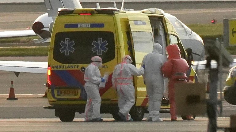 A sick cruise passenger wearing a hazmat suit is helped to a waiting ambulance at Amsterdam airport. 