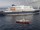 An aerial view of an ambulance boat carrying crew members wearing hazmat suits as they approach the pilot door on the starboard side of the cruise ship MV Hondius, while stationary off the port of Praia, the capital of Cape Verde, on May 5, 2026. Two seriously ill crew members on a cruise ship stricken by a deadly hantavirus outbreak will be evacuated via Cape Verde to the Netherlands, allowing the vessel to sail on to Spain's Canary Islands, the ship operator said Tuesday.
The MV Hondius has been at the centre of an international health scare since Saturday, when WHO was informed that the rare disease -- usually spread from infected rodents typically through urine, droppings and saliva -- was suspected of being behind the deaths of three of its passengers.
As others fell ill, passengers and crew have been in isolation after Cape Verde authorities barred the ship from docking, and as health authorities scrambled to find a port that would take the Hondius. (Photo by AFP)