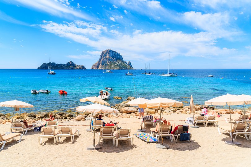 Tourists sunbathing on idyllic beach of Cala d'Hort, Ibiza island, Spain.
