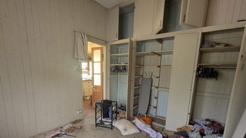 In a bedroom open wardrobes are seen with an ironing board inside and clothes and sheets on the floor.