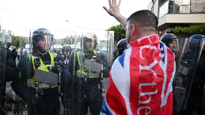 A man draped in a Union Flag stands in front of riot police as protesters gather near the location where Henry Nowak died.