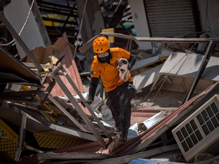 Ceedee, a rescue dog, is carried by a rescue worker as they search for survivors under the rubble of a building that collapsed following a magnitude 7.8 earthquake on June 09, 2026 in General Santos, Saranggani province, Philippines. 
