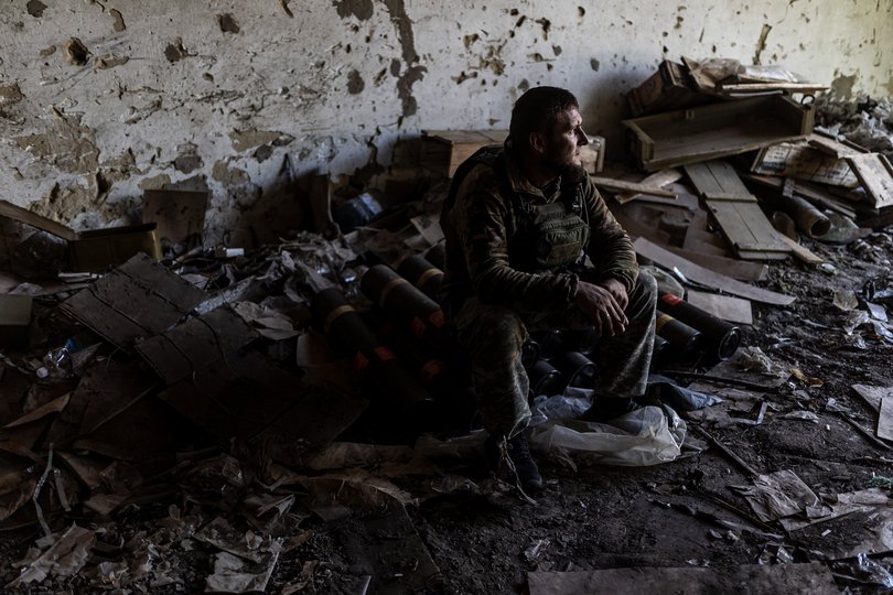 A Ukrainian soldier sits on shells while waiting for orders, in his fighting position in the direction of Chasiv Yar in Donetsk, 2024.