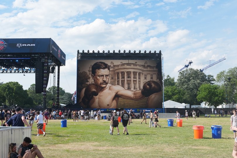 Artwork of President Theodore Roosevelt boxing is displayed on a screen as attendees gather.