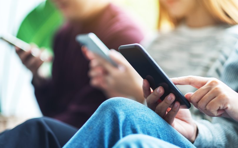 Group of young people using and looking at mobile phone while sitting together