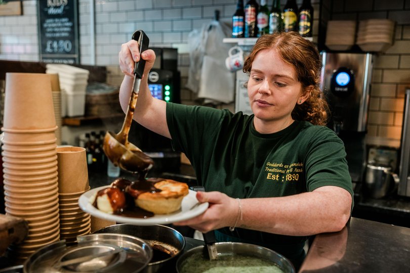 A worker douses a meal of pie and mash at Goddards. 