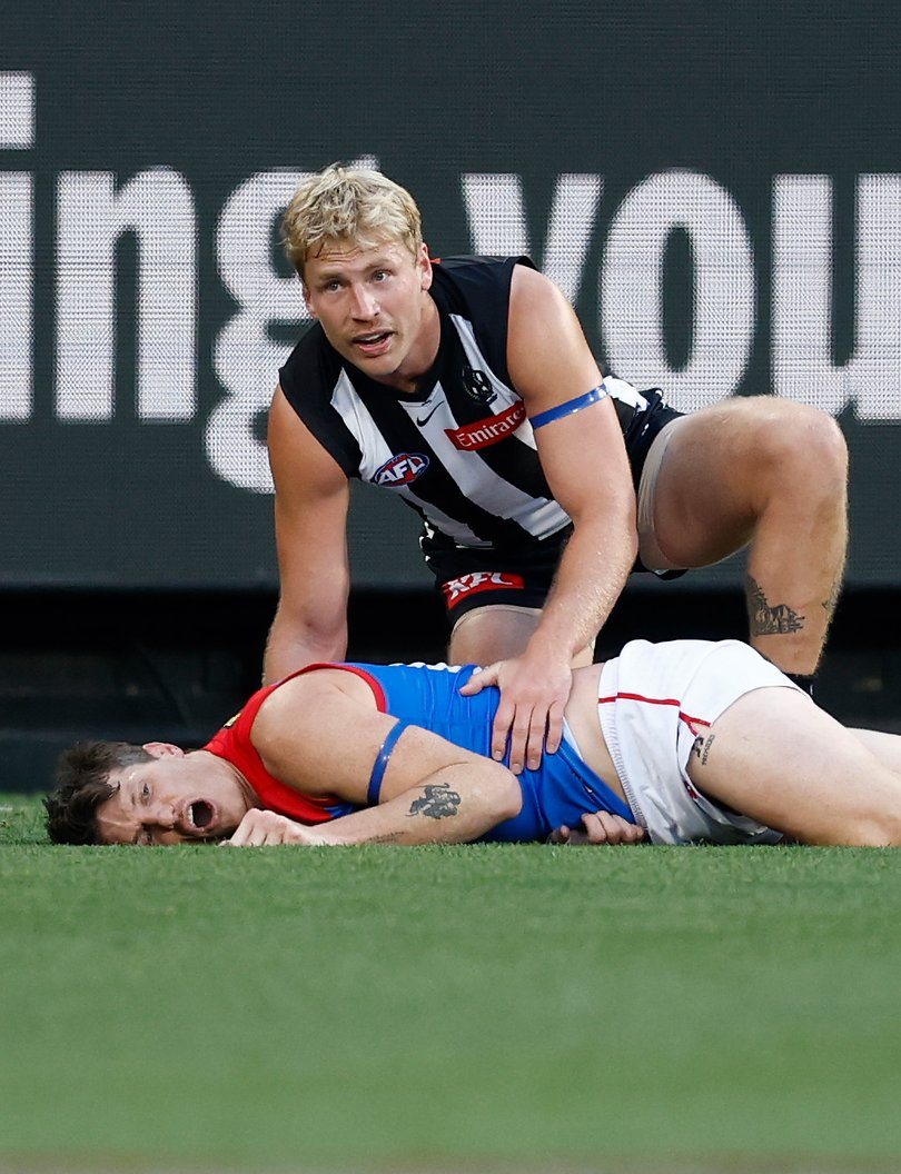 Brody Mihocek of the Demons lays injured as Billy Frampton of the Magpies looks on.