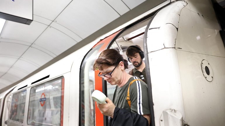 A commuter uses a fan in an attempt to cool down as they exit a London Underground tube carriage.
