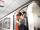 A commuter uses a fan in an attempt to cool down as they exit a London Underground tube carriage.