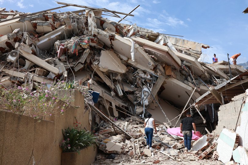 A man and a woman stand amid the rubble of a house. 