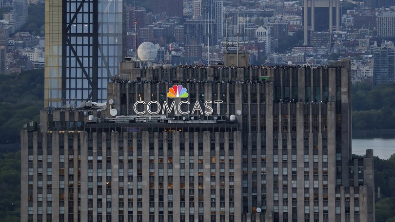 People visit the Top of the Rock observation deck behind a Comcast corporate logo at the top of 30 Rock in Rockefeller Center, New York.