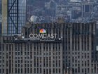 People visit the Top of the Rock observation deck behind a Comcast corporate logo at the top of 30 Rock in Rockefeller Center, New York.