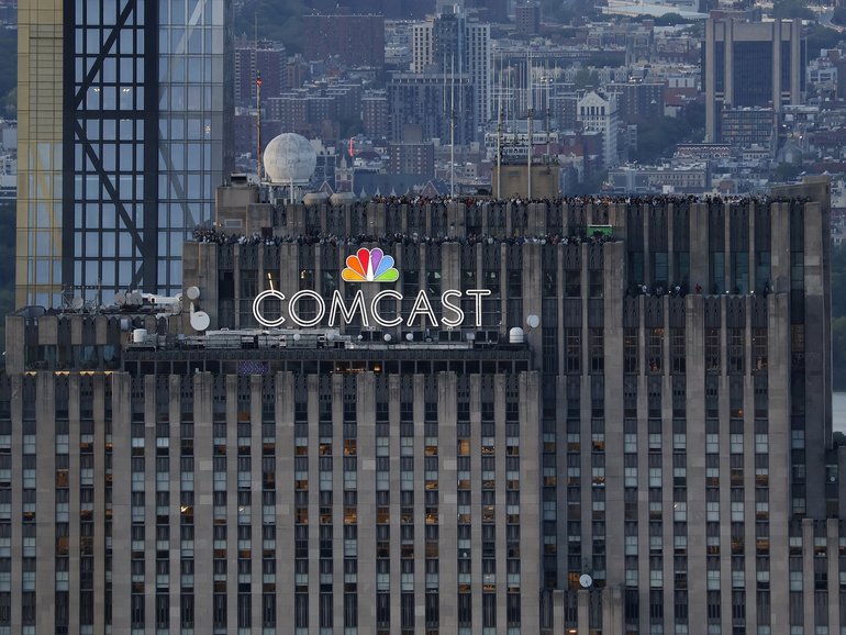 People visit the Top of the Rock observation deck behind a Comcast corporate logo at the top of 30 Rock in Rockefeller Center, New York.