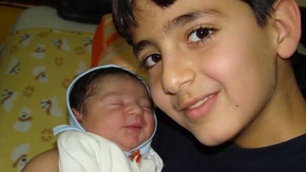 Nine-year-old Daniel Hidden holds his newborn brother Iliya in Iran.