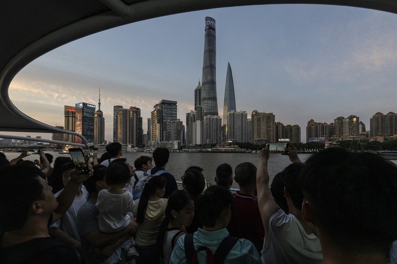 People take photos of the Shanghai skyline from the deck of a ferry crossing the Huangpu River in Shanghai. Rising fuel prices after the war in Iran added pressure on Chinese households, curbing travel and spending. 