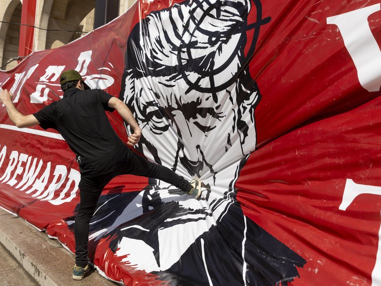 An Iranian kicks a large banner depicting Donald Trump during funeral ceremonies for Iran's slain Supreme Leader, Ayatollah Ali Khamenei.