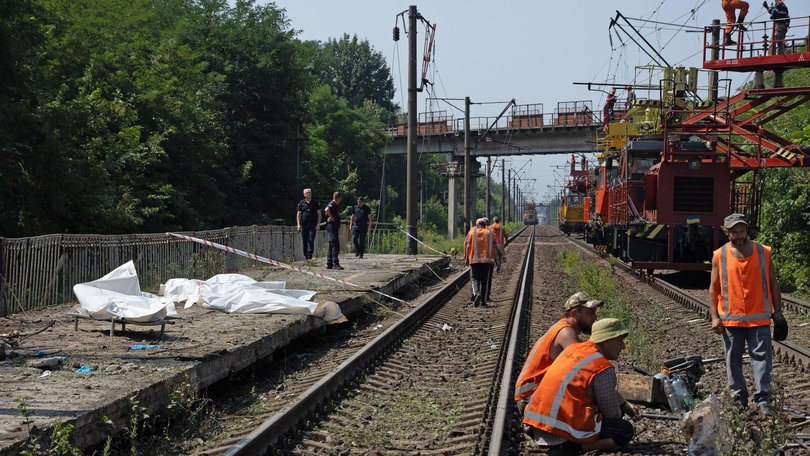 Bodies lie in body bags on a railway platform at the site of a Russian strike, while electricians repair a damaged power line nearby.