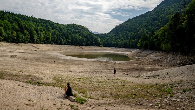 People walk along the exposed lake bottom of the severely shrunk Nussensee mountain lake during ongoing drought in Austria.