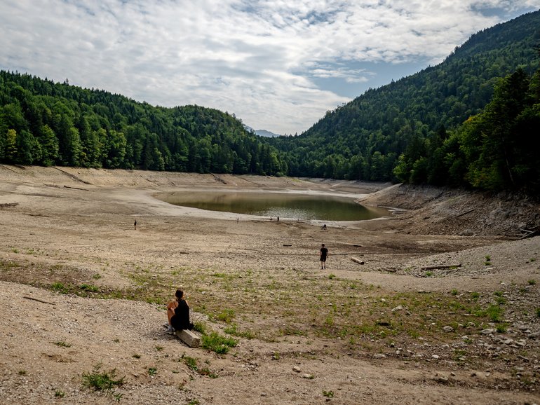 People walk along the exposed lake bottom of the severely shrunk Nussensee mountain lake during ongoing drought in Austria.