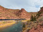 The scenes are picturesque as the train zig-zags through towering red cliffs over water.