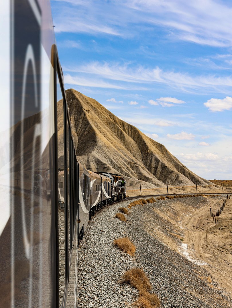 The train hugs the cliff edge, the river flashing below, walls of rust, oxblood and blackened rock rising close on either side.
