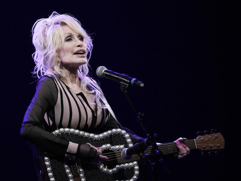 Dolly Parton with a bedazzled guitar, part of her signature look.