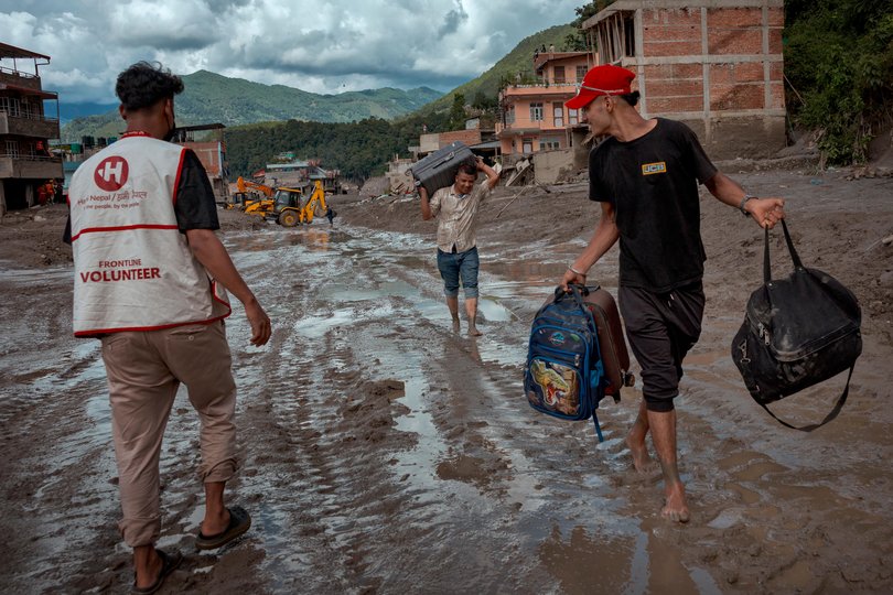 Residents carry their belongings along a road heavily covered in mud following flash floods on August 27, 2026 in Trishuli, Nepal.