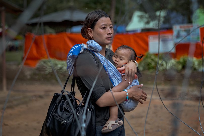 A woman carrying a baby waits for news on missing loved ones at a military camp.