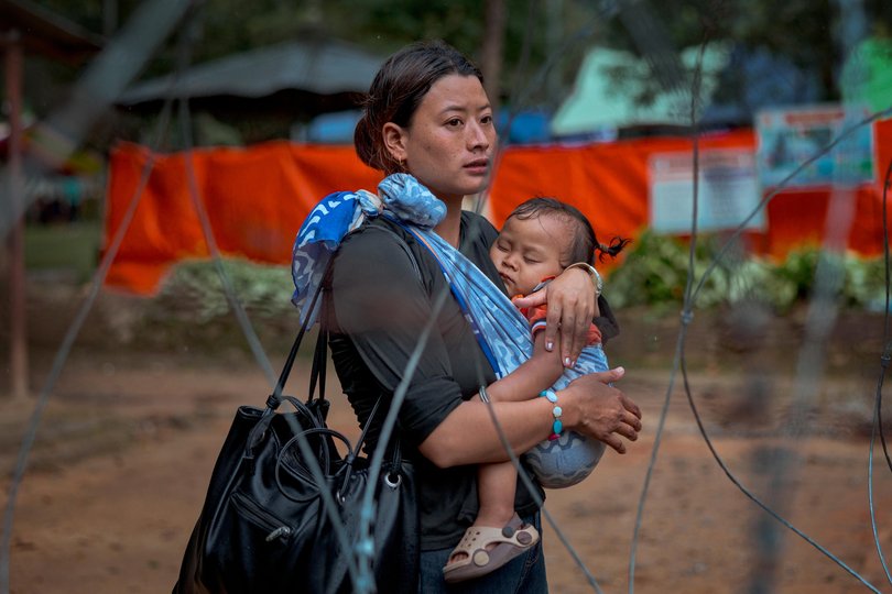 A woman carrying a baby waits for news on missing loved ones at a military camp in Trishuli, Nepal.