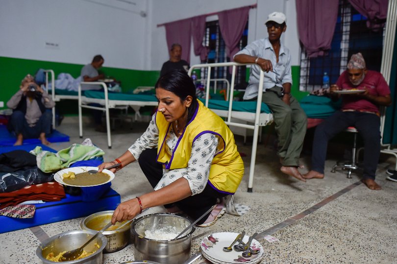 A volunteer serves food to elderly people of old age home of devikot at a makeshift flood relief camp inside a hospital.