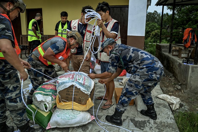 Volunteers work with police to pack essential food, medicine, and other supplies for a drone relief operation at Devighat, Nepal on Saturday, Aug. 29, 2026. The drone was used to transport goods across a river to residents who are left stranded and completely cut off. (Atul Loke/The New York Times)