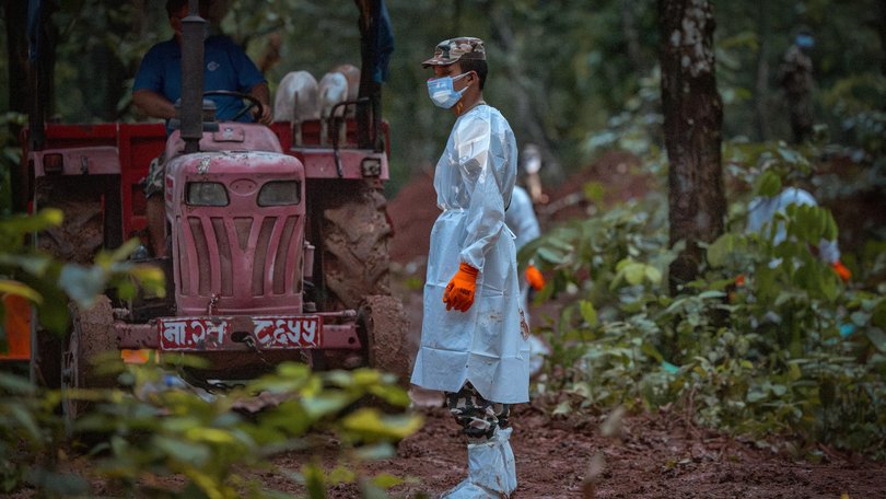 An army soldier stands by in a hazmat suit as unidentified bodies recovered from the flash floods are buried at a mass burial site in Nepal.