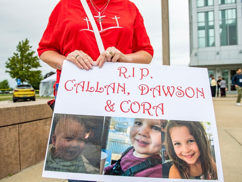 A woman carries a sign remembering the three murdered children outside the court.