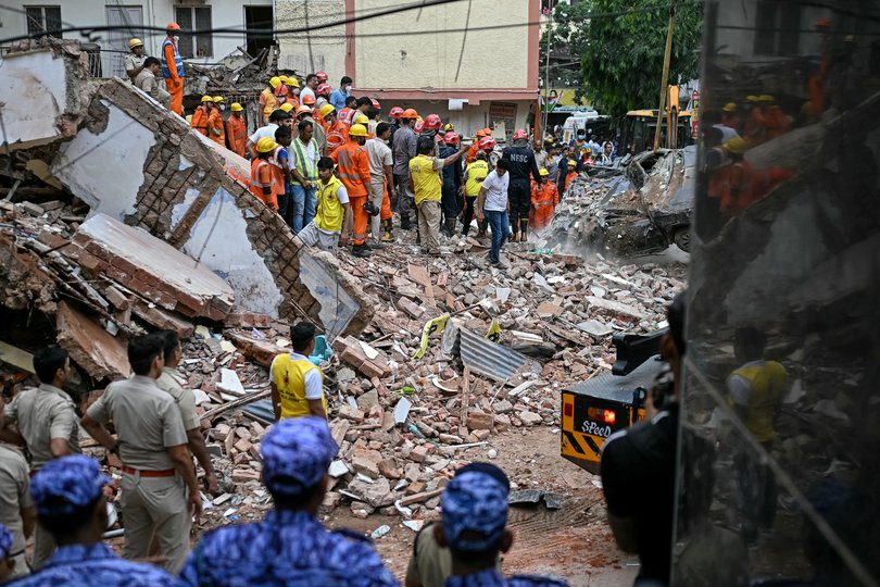 Security personnel stand guard as rescue personnel conduct a search operation for survivors at the site of a building collapse in the Satya Niketan area in New Delhi on September 6, 2026. 