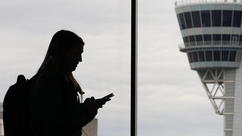A traveler with a smartphone walks past an air traffic control tower at Philadelphia International Airport.