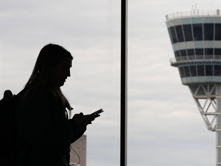A traveler with a smartphone walks past an air traffic control tower at Philadelphia International Airport.