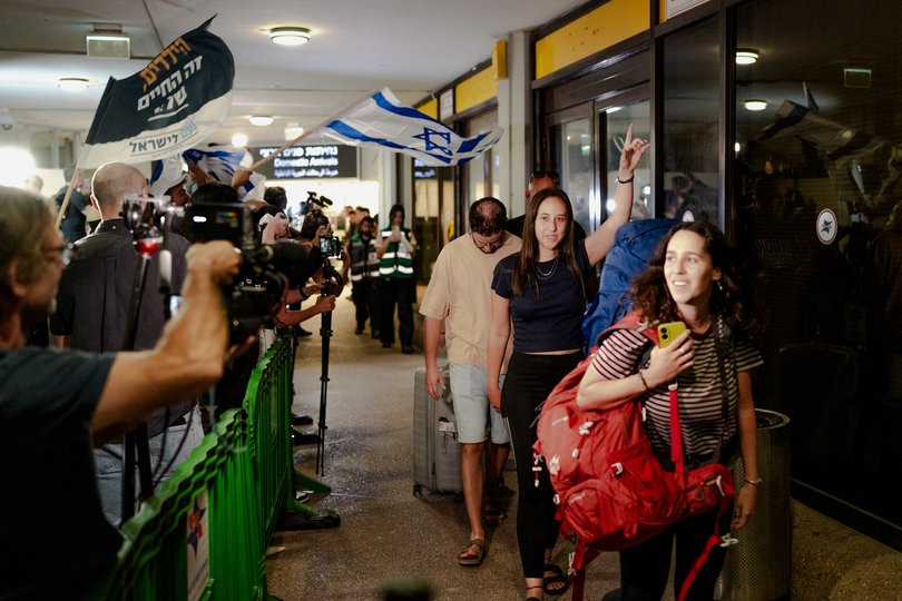 Passengers carry luggage through the terminal corridor lined with waiting crowds and flags upon arriving on a Flydubai retrieval flight at Ben Gurion Airport on September 30, 2026 in Tzafria, Israel.