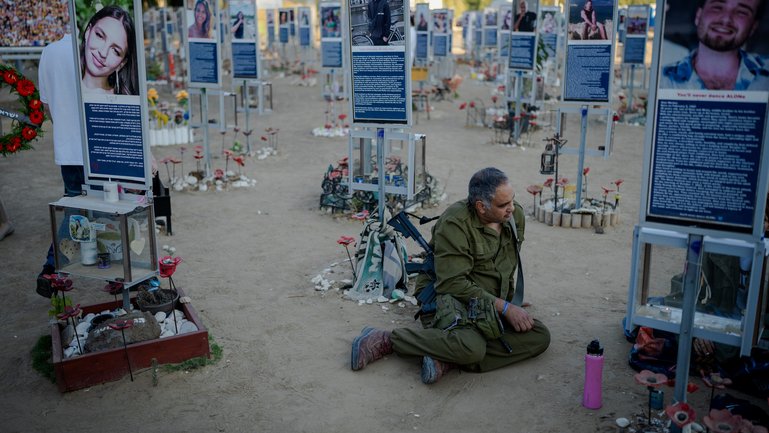 An armed Israeli soldier sits on the ground beside memorial markers at the Nova music festival site as Israel marks the third anniversary of the Oct. 7th 2023 attacks.