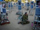 An armed Israeli soldier sits on the ground beside memorial markers at the Nova music festival site as Israel marks the third anniversary of the Oct. 7th 2023 attacks.