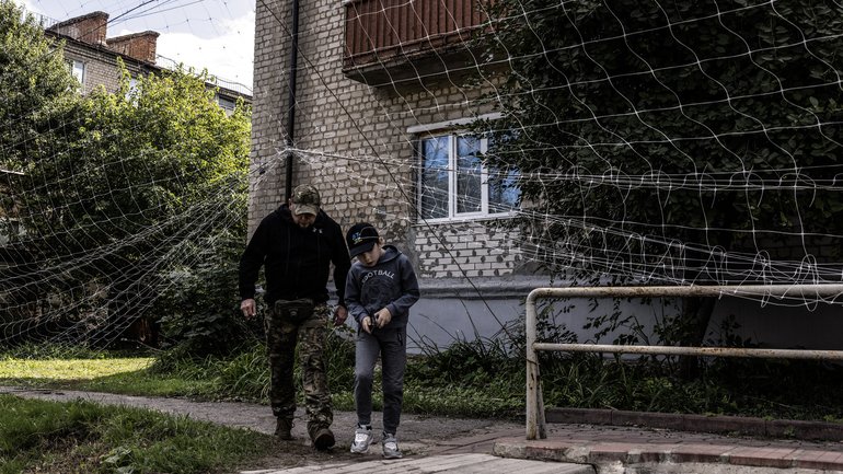 A man in a Ukrainian military uniform and a boy pass under protective netting.