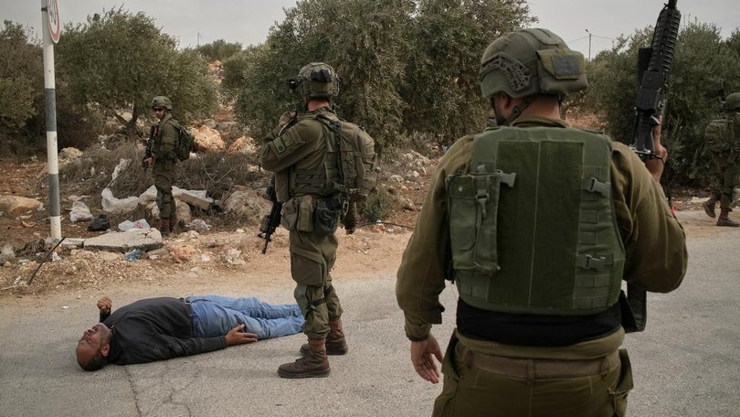 Israeli soldiers stand beside a Palestinian man after soldiers shot him following a settler attack. (AP PHOTO)