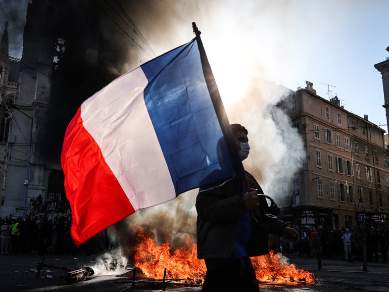 A protester waving a French national flag walks past a fire during clashes prior to the start of a demonstration in Marseille, southern France.