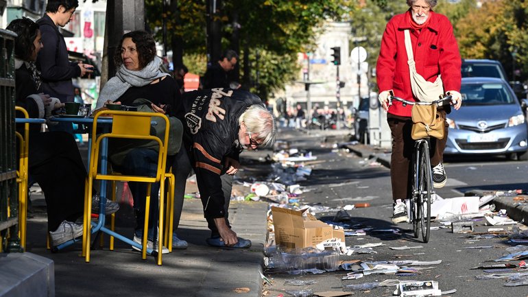 Residents sit outside at a cafe as a cyclist passes by among damages in Paris on October 18, 2026, a day after nationwide protests against the "high cost of living". France's Prime Minister Sebastien Lecornu said 1,200 people were arrested in protests across the country on October 17, and 150 police were hurt as Clashes between police and protesters, massive looting and multiple blazes gripped France as nationwide marches against soaring inflation degenerated into street violence of "extreme intensity". (Photo by Matthieu RONDEL / AFP)