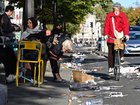 Residents sit outside at a cafe as a cyclist passes by among damages in Paris on October 18, 2026, a day after nationwide protests against the "high cost of living". France's Prime Minister Sebastien Lecornu said 1,200 people were arrested in protests across the country on October 17, and 150 police were hurt as Clashes between police and protesters, massive looting and multiple blazes gripped France as nationwide marches against soaring inflation degenerated into street violence of "extreme intensity". (Photo by Matthieu RONDEL / AFP)