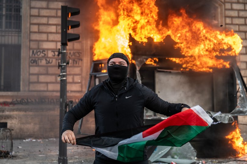A protester holds a Palestinian flag as a bus stop burns during a demonstration at Place de Republique on October 17, 2026 in Paris, France. 