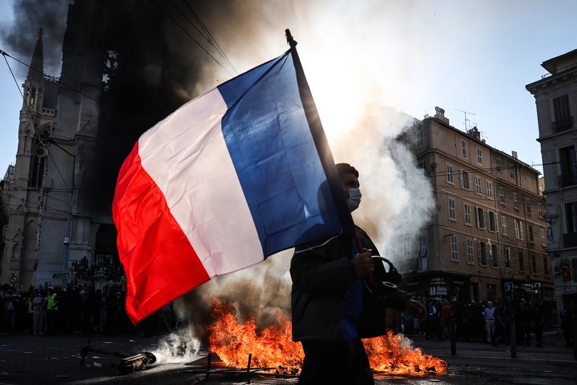 A protester waving a French national flag walks past a fire during clashes prior to the start of a demonstration.