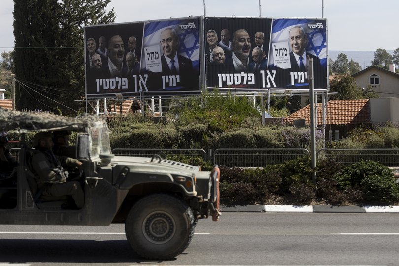 An Israeli army vehicle passes by an election campaign banner featuring Israeli Prime Minister, and leader of Likud party, Benjamin Netanyahu.