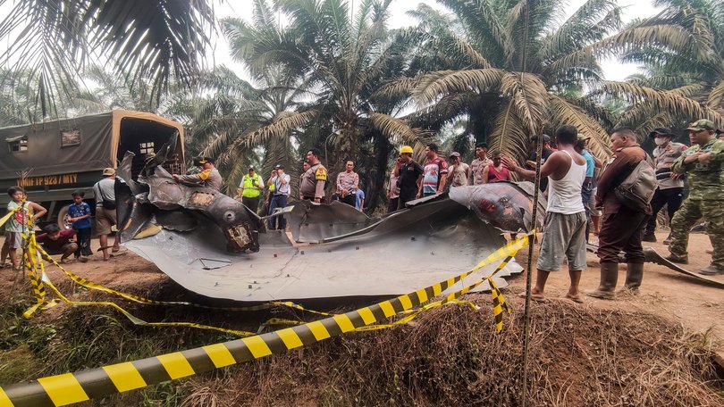Residents, plantation workers, and security officials gather around a large charred metallic fragment, suspected to be rocket debris, at an oil palm plantation in East Kotawaringin Regency, in Indonesia's Central Kalimantan province. Indonesian authorities were investigating after a piece of rocket the size of a car crashed into an oil palm plantation on Indonesian Borneo.